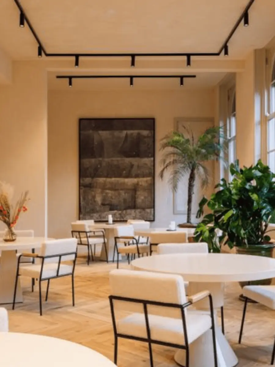 Light-filled dining room with round tables, cream chairs and large plants